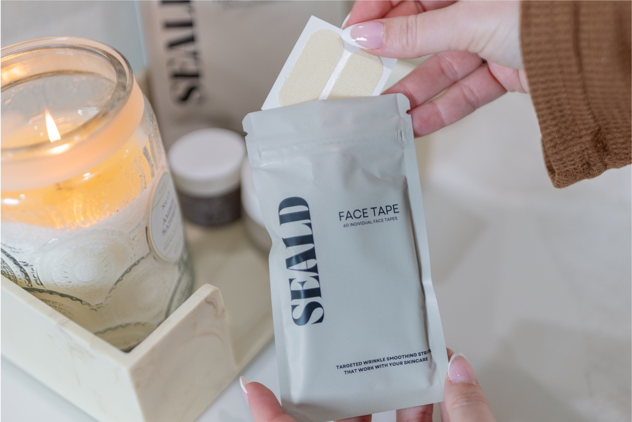Hand holding a package of 'SEALD' face tape with a candle in the background