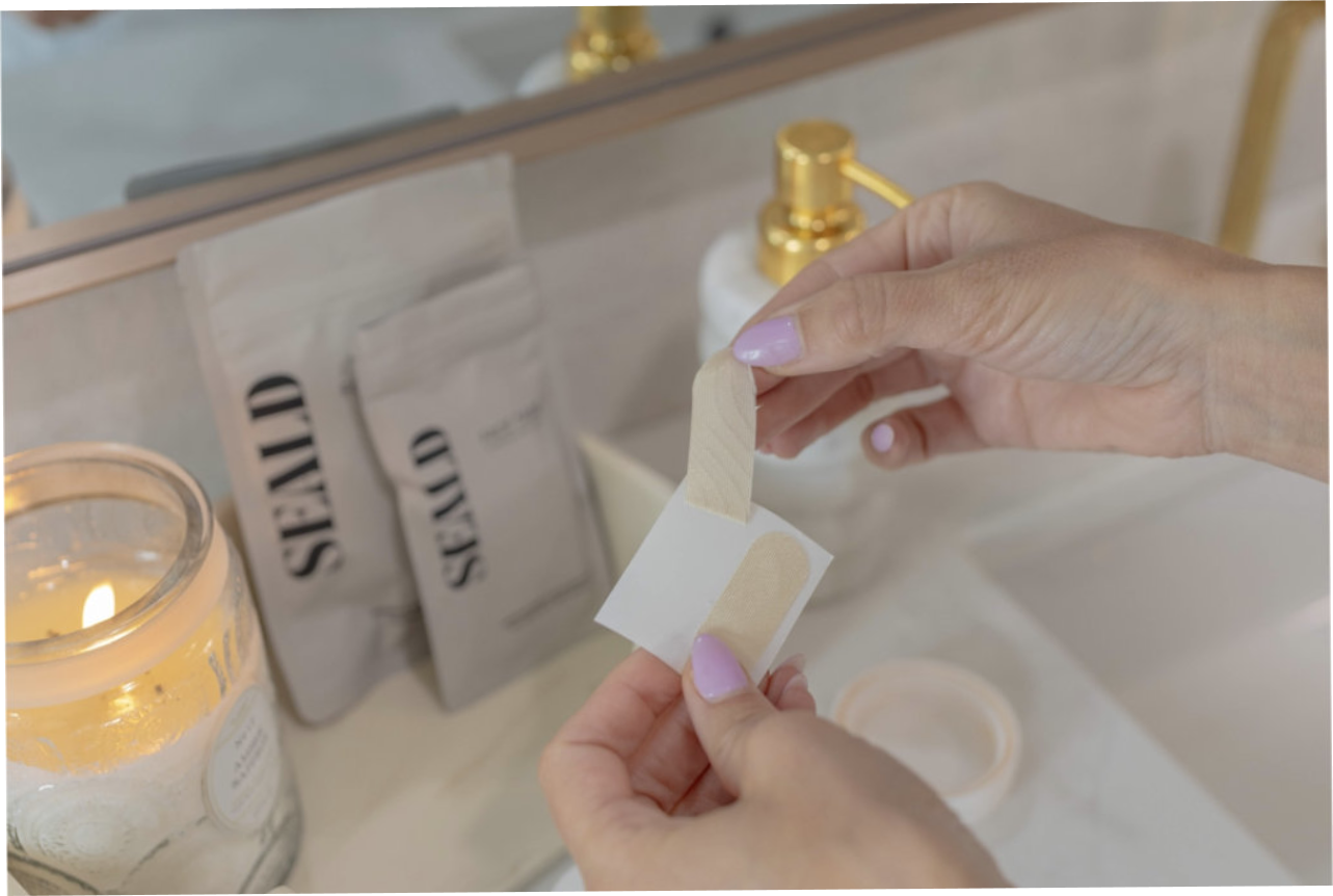 Person holding a seald face tape over a sink with a candle and seald packaging in the background