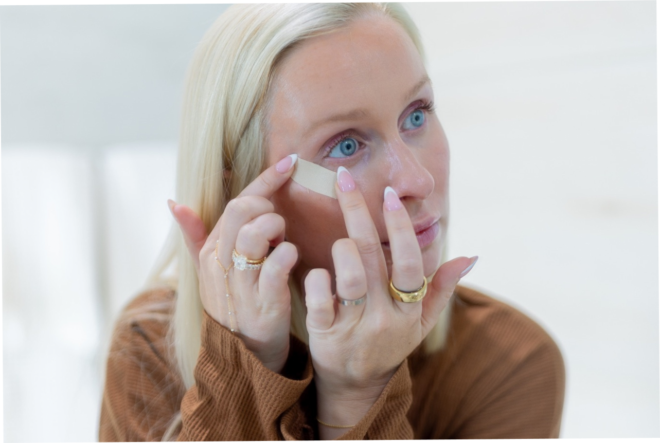 Woman applying a seald face tape to her face with a white background