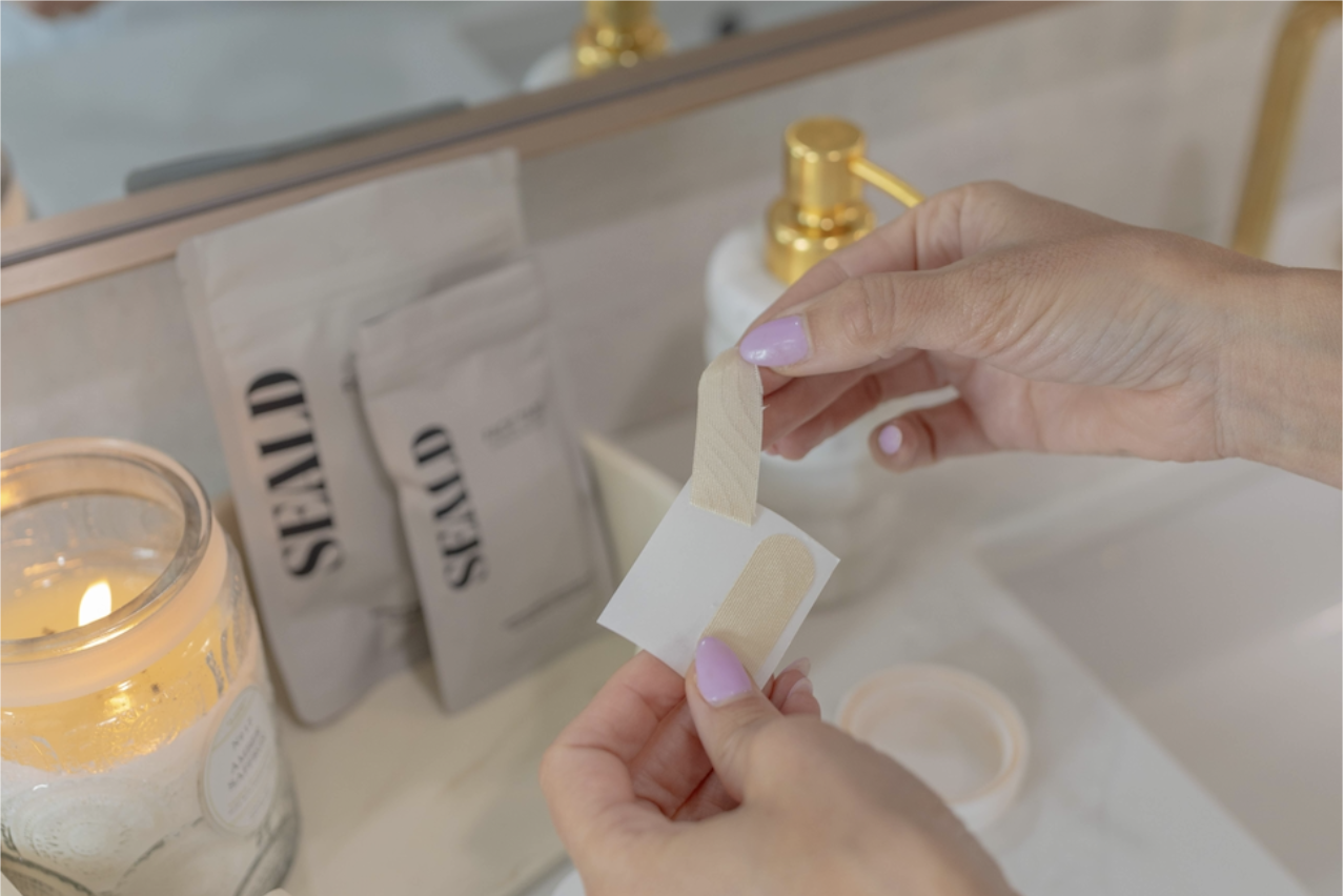 Person applying a bandage to a cut on a bathroom counter with a candle and soap in the background.