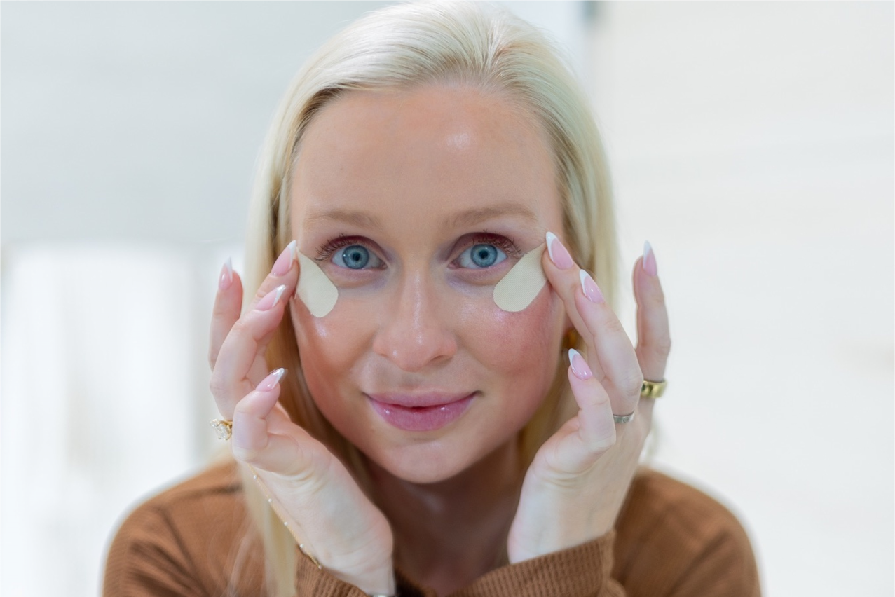 Woman applying eye patches with a neutral background