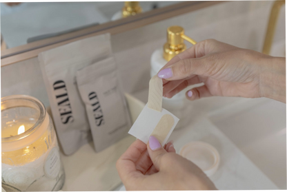 Person holding a seald face tape over a sink with a candle and seald packaging in the background