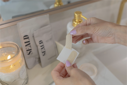 Person applying a bandage to a cut on a bathroom counter with a candle and soap in the background.